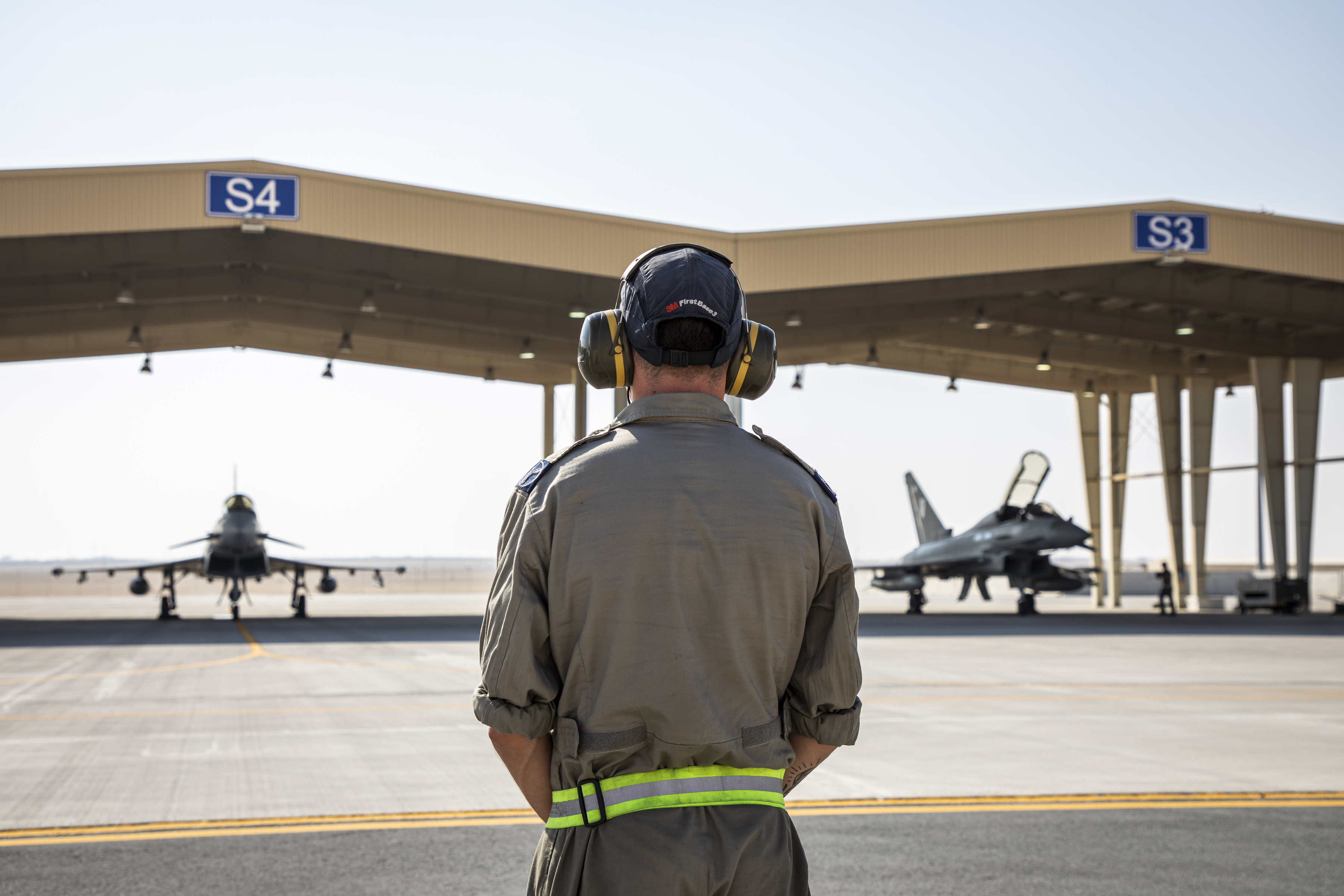 Image shows personnel on the airfield with fighter jets under hangars.